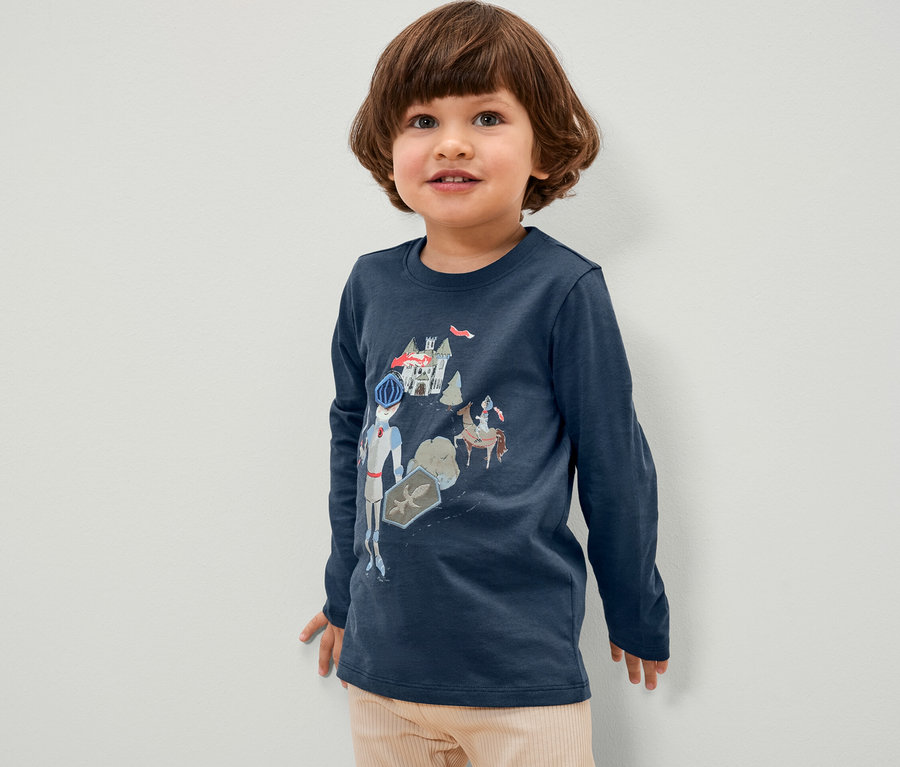 Junge trägt ein blaues Langarmshirt mit Ritter-Motiv.