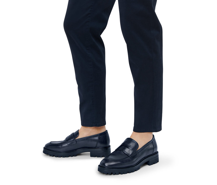 Beine einer Person in marineblauen Hosen und Leder-Loafern.