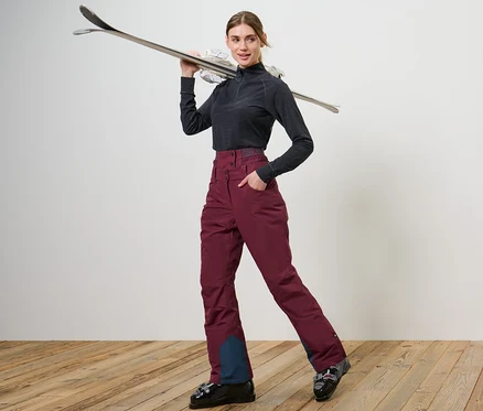 Frau posiert in Skischuhen und weinroten Ski- und Snowboardhose.