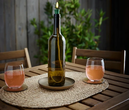 Auf einem Holztisch stehen eine LED-Flaschenleuchte »Candle« und zwei Gläser mit Getränk.