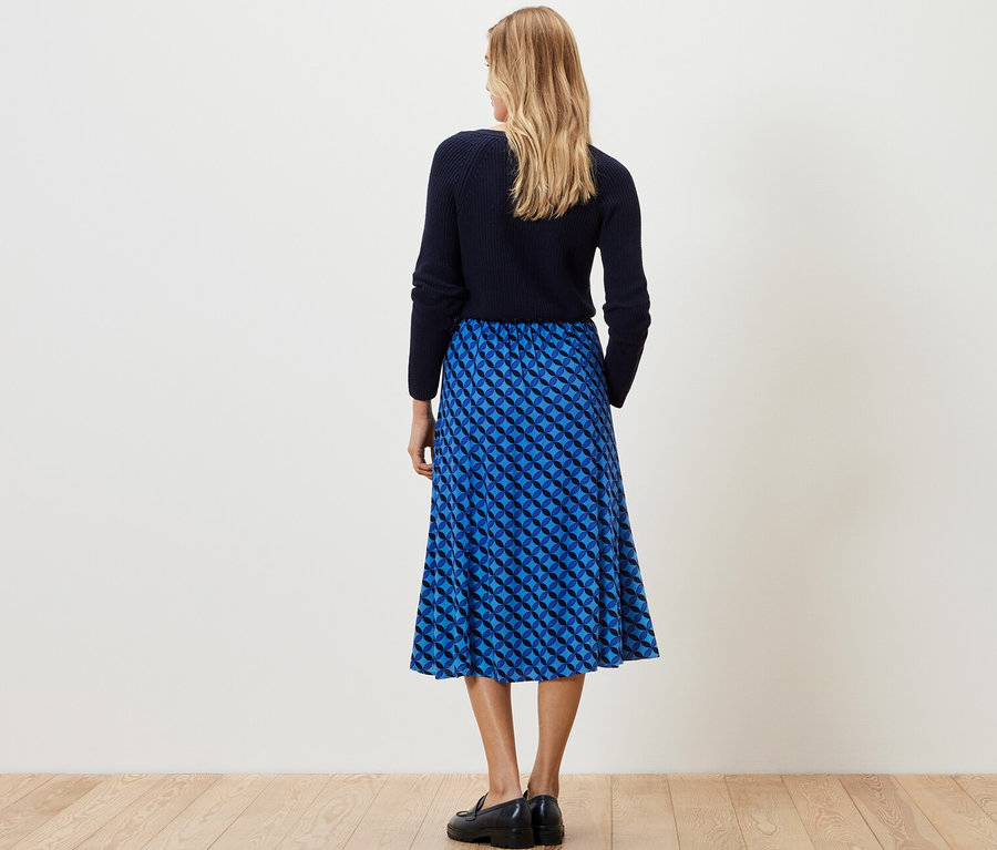 Eine Frau steht mit dem Rücken zur Kamera und trägt einen dunkelblauen, bedruckten Midirock.