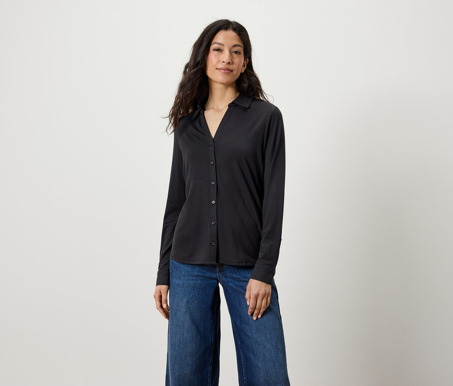 Eine Frau trägt ein schwarzes Langarmhemd und blaue Jeans.