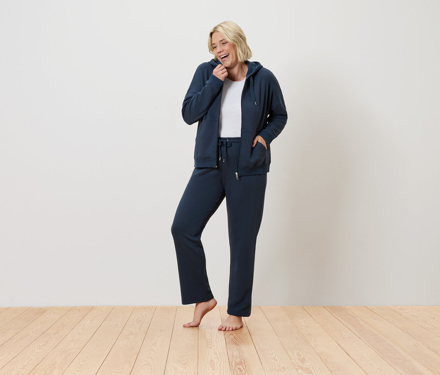 Frau steht und lächelt, sie trägt einen blauen Trainingsanzug.