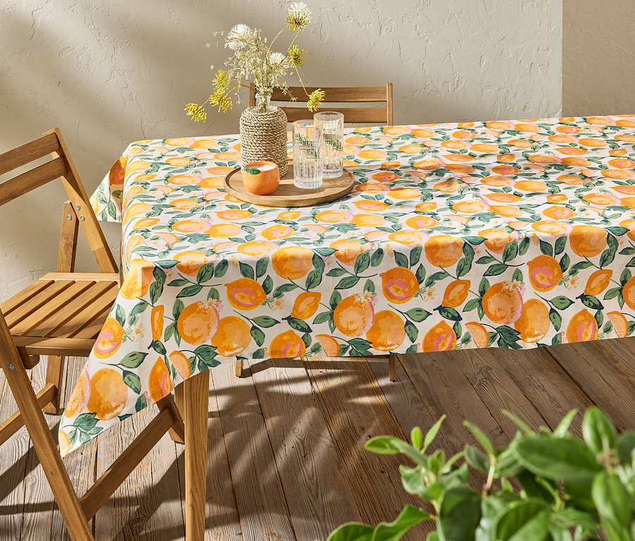Tisch mit abwischbarer Tischdecke mit Zitrusmuster, darauf Vase mit Blumen und Wassergläser.