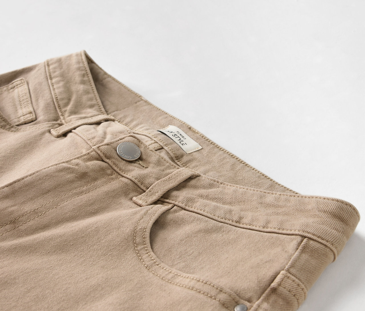 Detailaufnahme einer beigen Hose mit Knopf und Tasche.