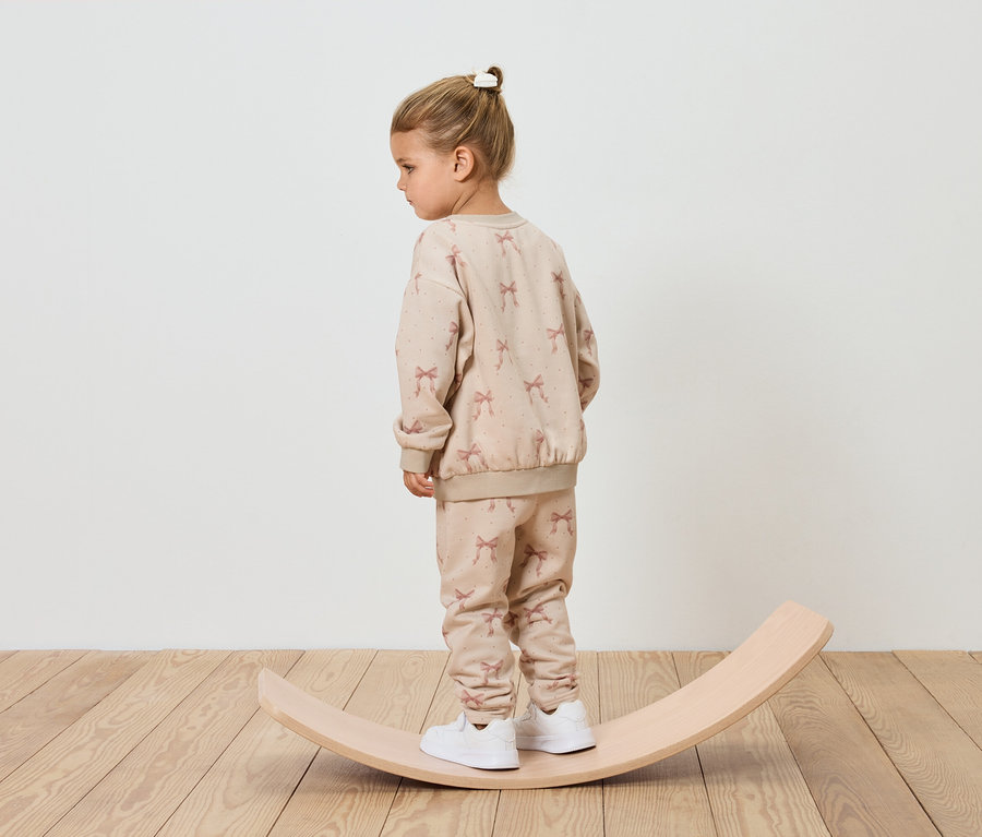 Mädchen im beige Trainingsanzug steht auf einem hölzernen Balancebrett.