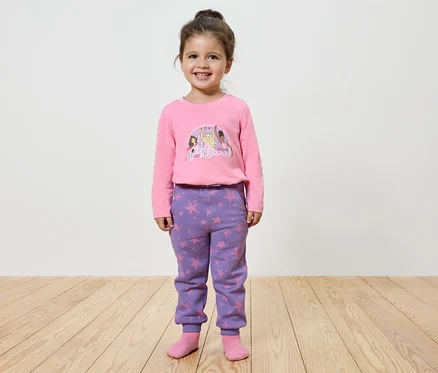 Lächelndes kleines Mädchen posiert in einem rosa bedruckten Langarmshirt und lila Sternen-Hosen.
