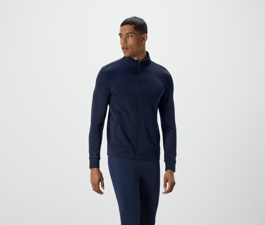 Mann in dunkelblauer Reißverschlussjacke und Hose blickt nach links.