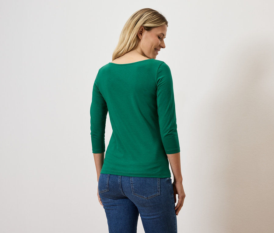 Frau schaut zur Seite und trägt ein grünes Dreiviertelarm-T-Shirt und Jeans.