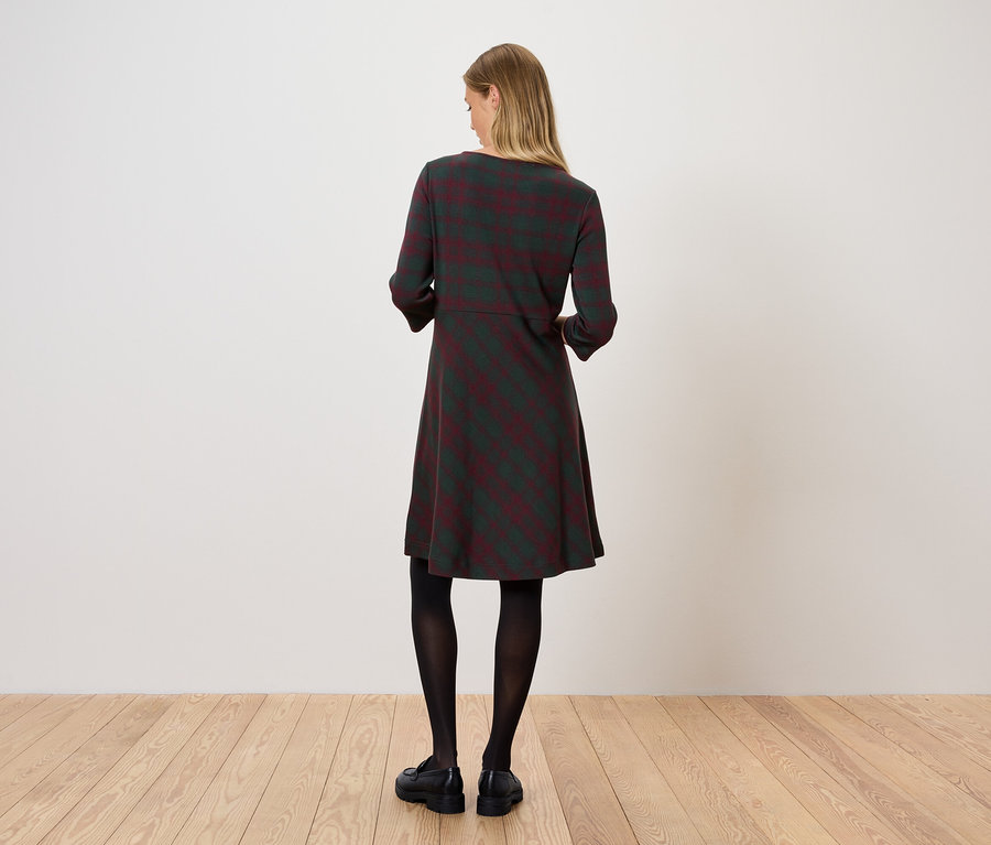 Eine Frau steht mit dem Rücken zur Kamera und trägt ein gestreiftes Kleid, schwarze Strumpfhosen und schwarze Schuhe.
