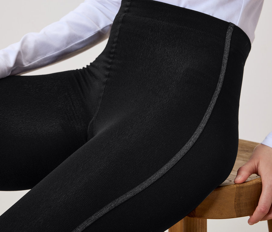 Frau sitzt auf einem Holzhocker und trägt eine schwarze Leggings mit einem grauen Streifen an der Seite.