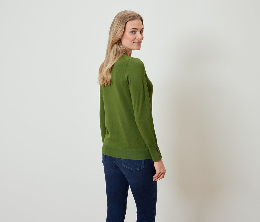 Eine Frau blickt über ihre Schulter, sie trägt einen olivgrünen Pullover und dunkelblaue Jeans.