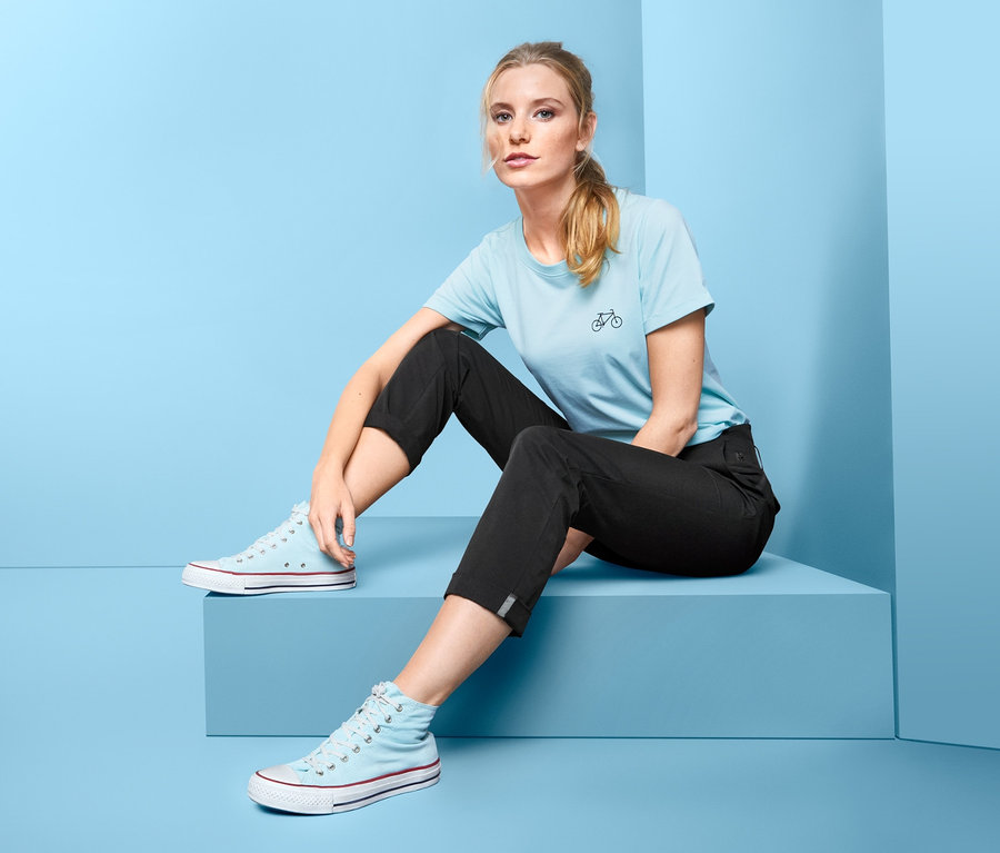 Eine Frau sitzt vor blauem Hintergrund und trägt eine Funktionshose.