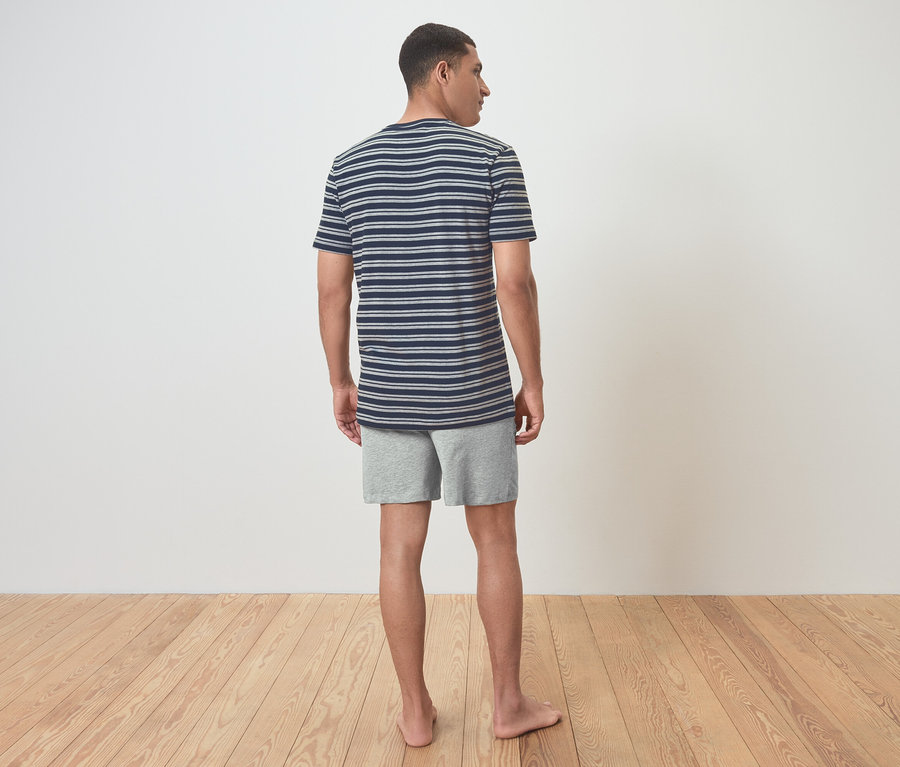 Mann mit gestreiftem T-Shirt und Shorts steht mit dem Rücken zur Kamera.