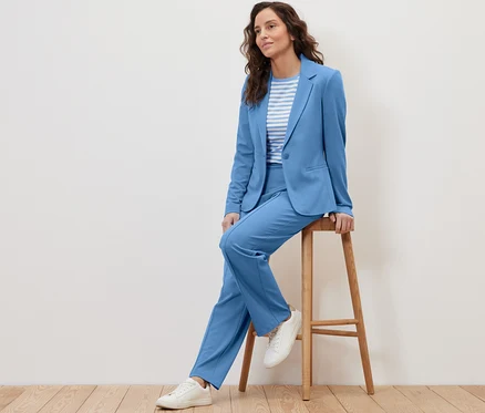 Eine Frau sitzt auf einem Hocker und trägt einen hellblauen Jerseyblazer.