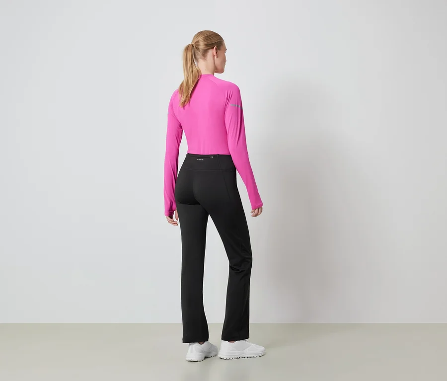 Frau mit dem Rücken zur Kamera trägt ein pinkes Langarmshirt und eine schwarze Hose.