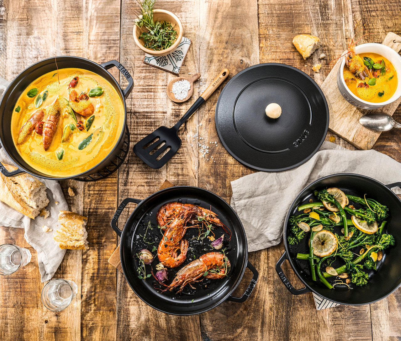 Draufsicht auf rustikalen Holztisch mit Speisen, darunter ein STAUB Kochtopf-Set »La Cocotte«, 3-teilig, mit Suppe und Garnelen.
