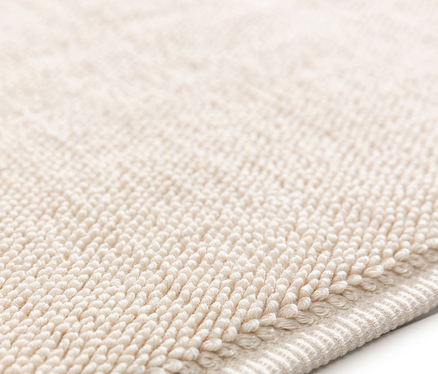 Nahaufnahme eines beigen Badteppichs mit Schlingenstruktur.