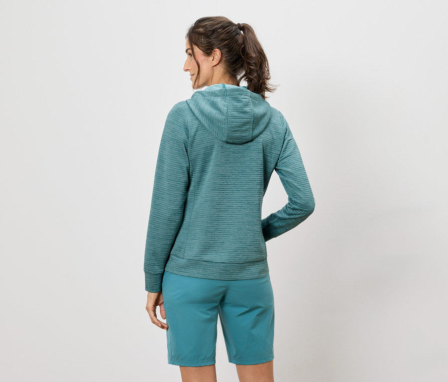 Eine Frau steht mit dem Rücken zur Kamera und trägt einen blaugrünen Hoodie und Shorts.