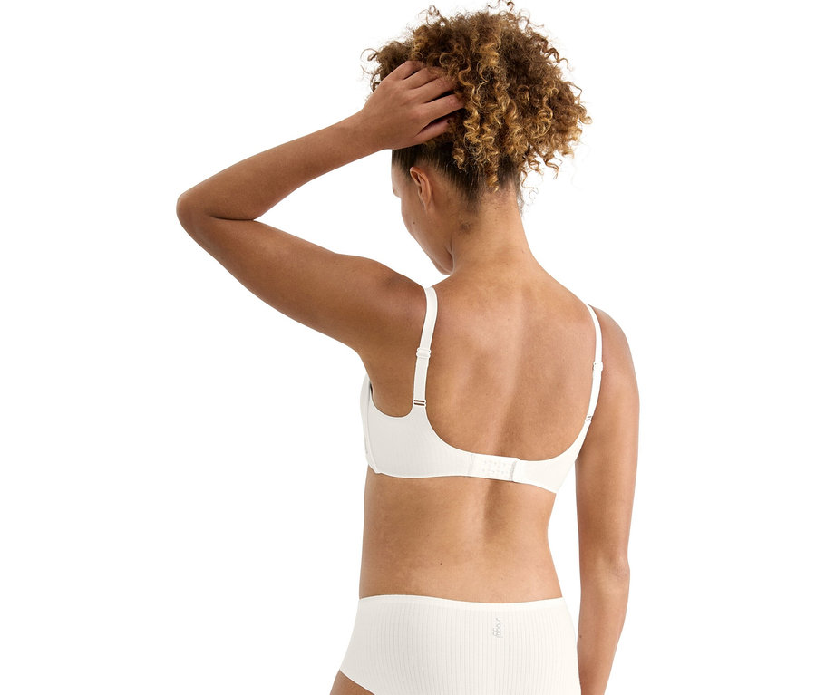 Rückansicht einer Frau mit lockigem Haar, die einen weißen BH und Slip trägt und ihre Hand im Haar hat.