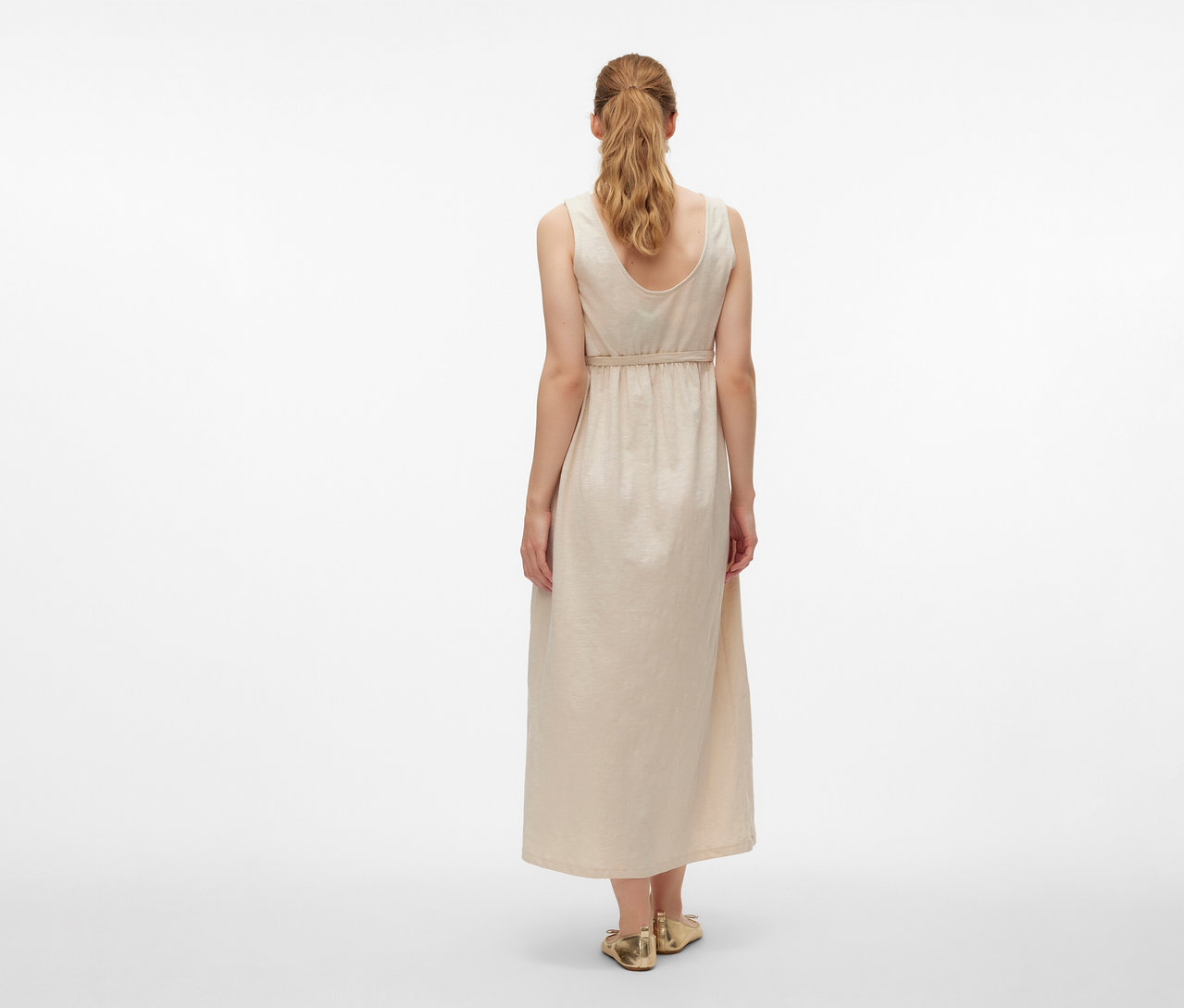 Rückansicht einer Frau im MAMALICIOUS Schwangerschaftskleid »MLEVI LIA« und goldenen Schuhen vor einem weißen Hintergrund.