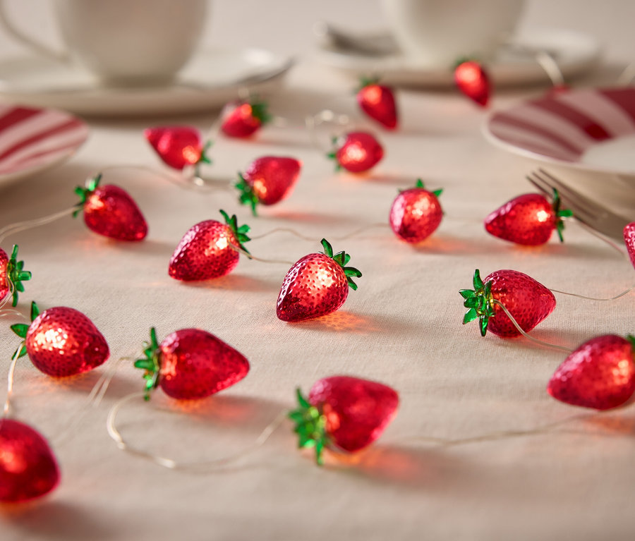 Erdbeer-Lichterkette auf einem Tisch mit Geschirr.