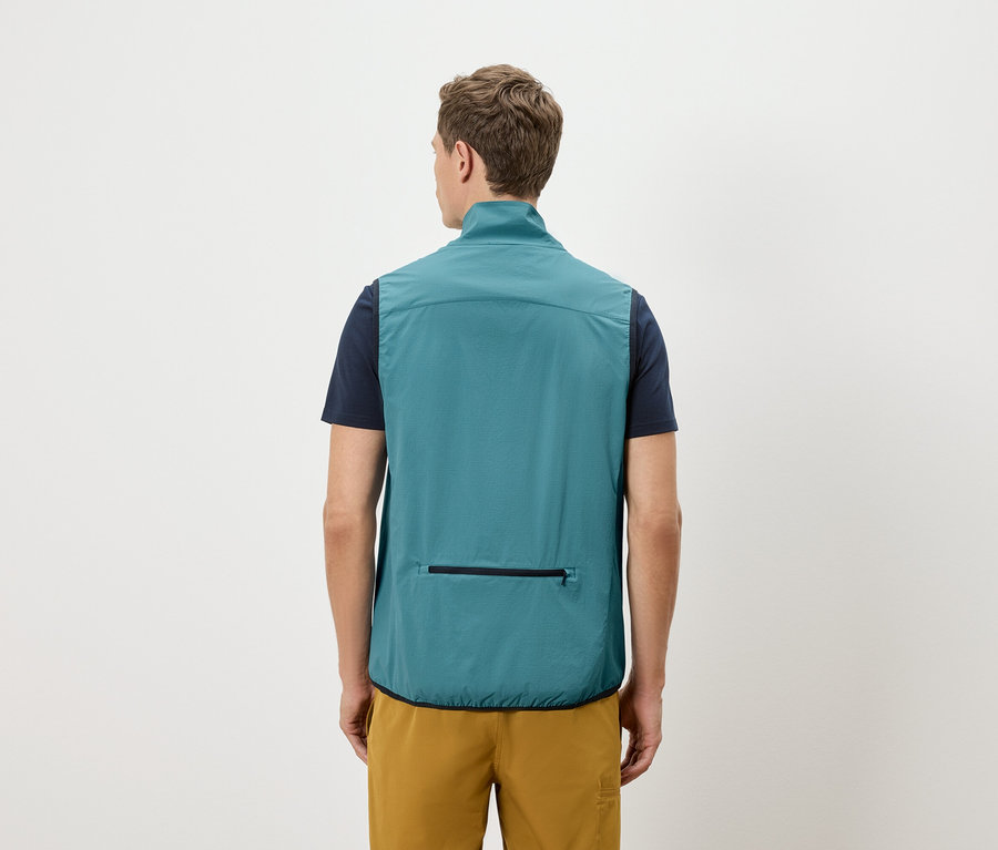 Mann von hinten in marineblauem T-Shirt und goldener Shorts, trägt eine petrolfarbene Weste mit Reißverschlusstasche.