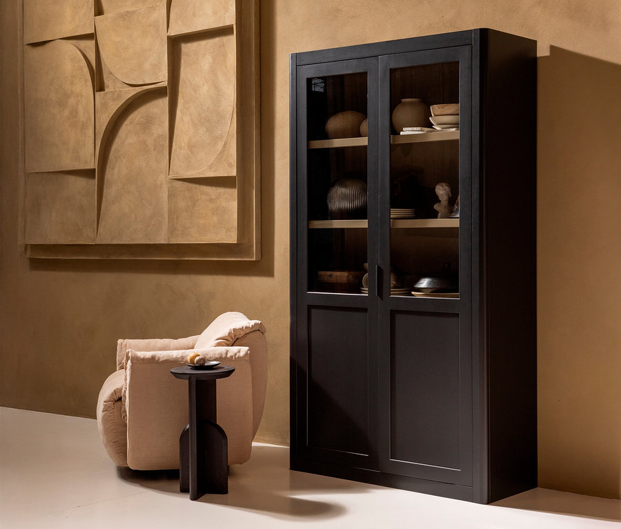 Schwarzer Glasschrank steht neben einem beigen Sessel und einem kleinen Tisch, an der Wand hängt ein abstraktes Kunstwerk.