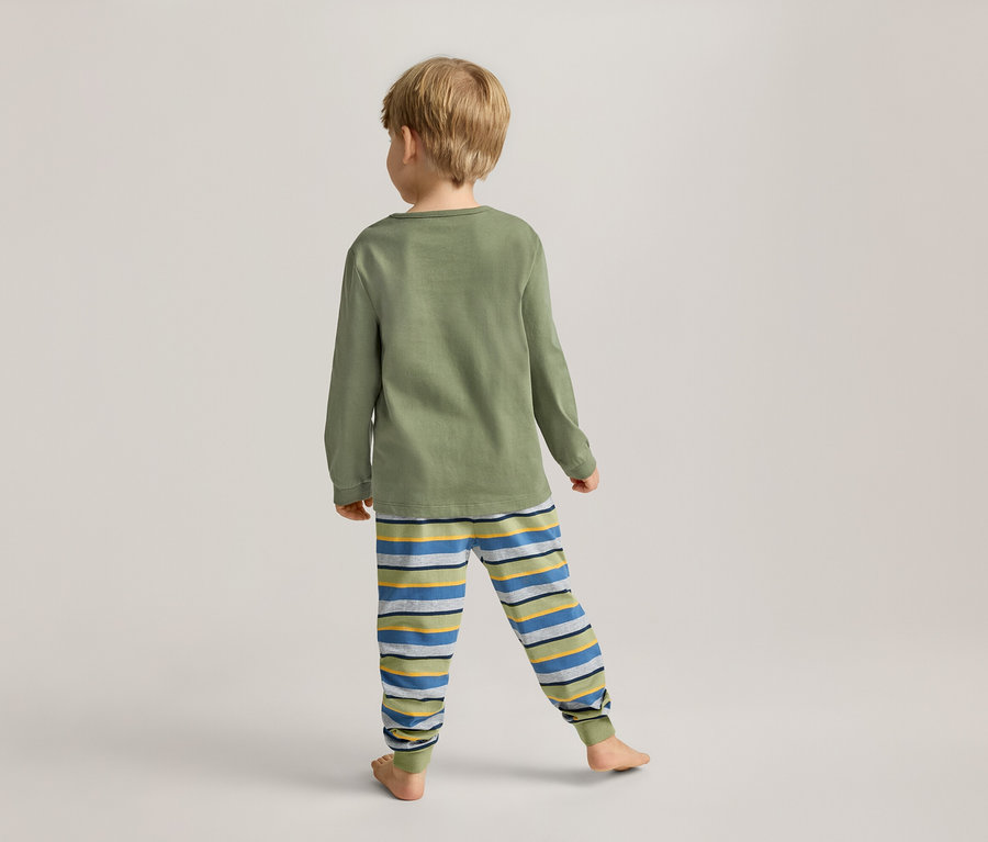 Ein Kind mit blonden Haaren steht mit dem Rücken zum Betrachter und trägt ein grünes Langarmshirt und gestreifte Hosen.