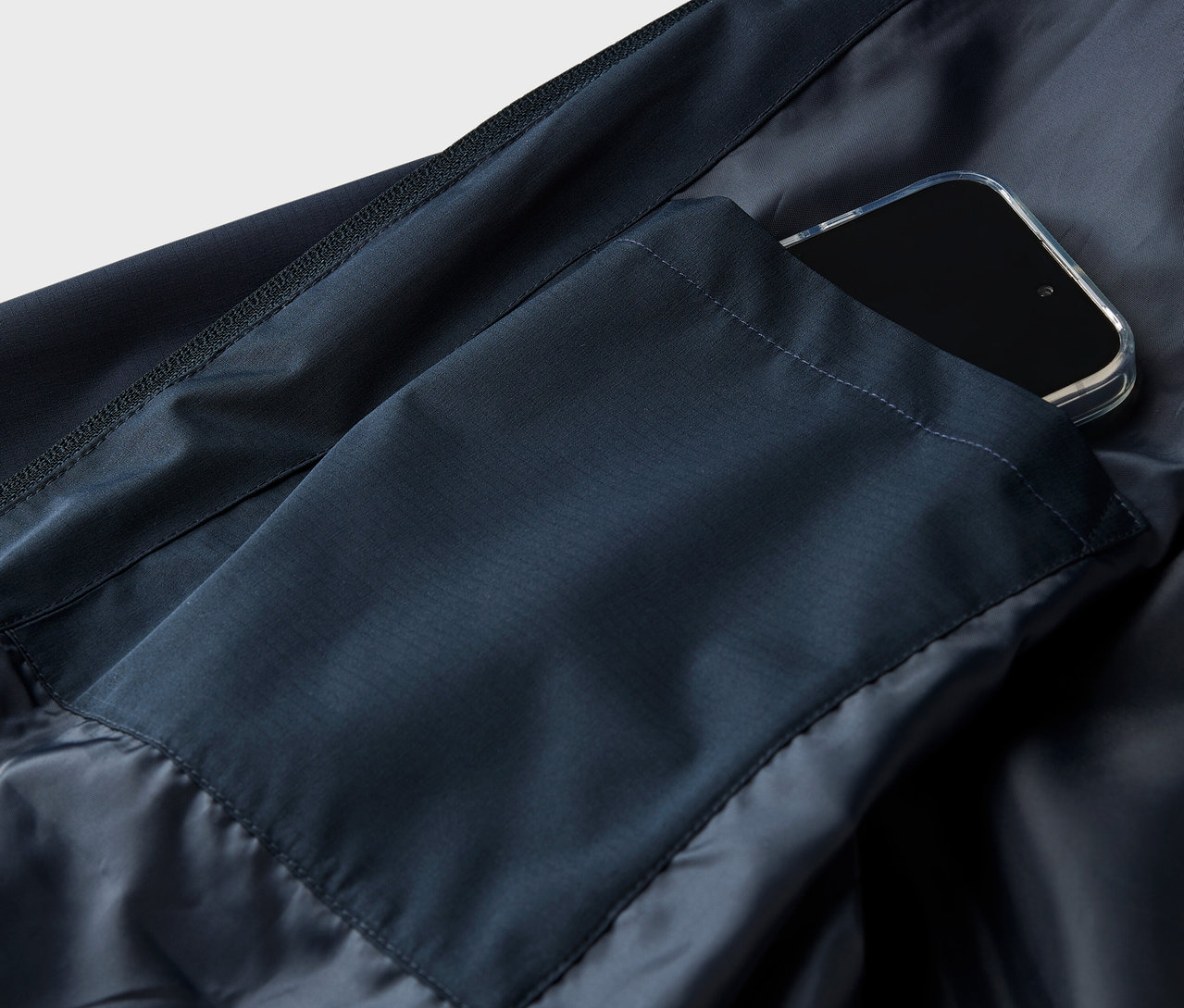 Detailaufnahme einer marineblauen Jacke mit einem Smartphone in der Tasche.