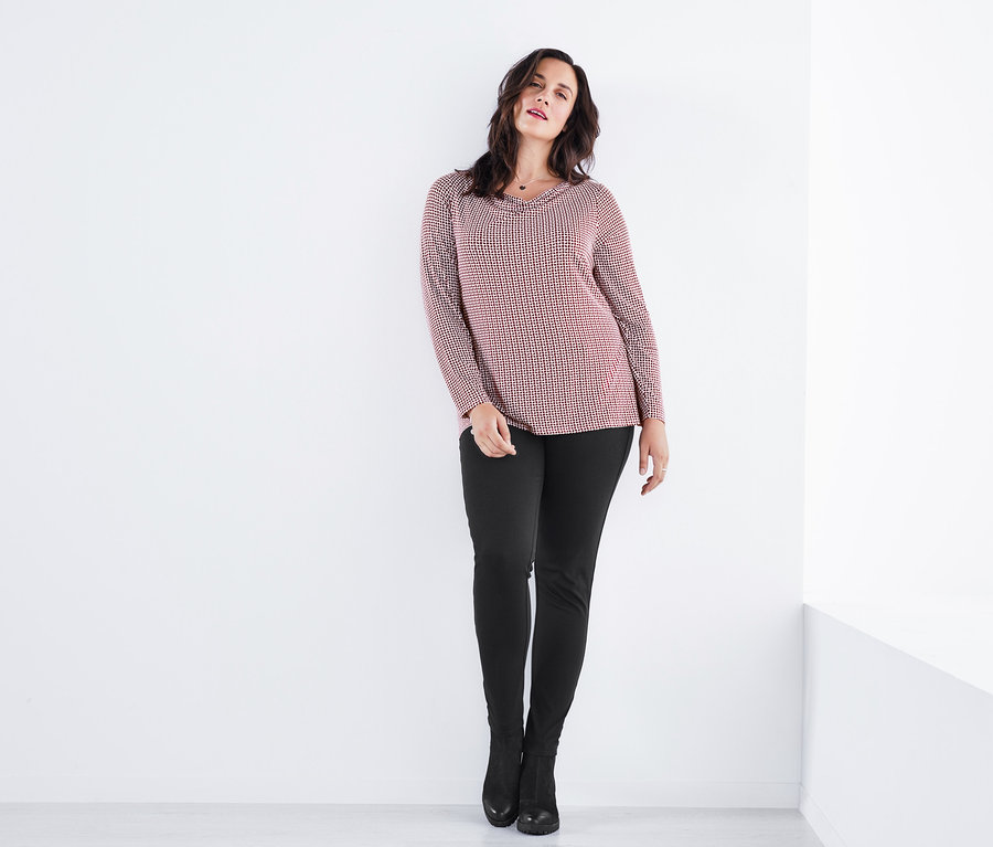 Frau posiert in einem Shirt mit Wasserfall-Ausschnitt, Jeggings und Leder-Stiefeletten.