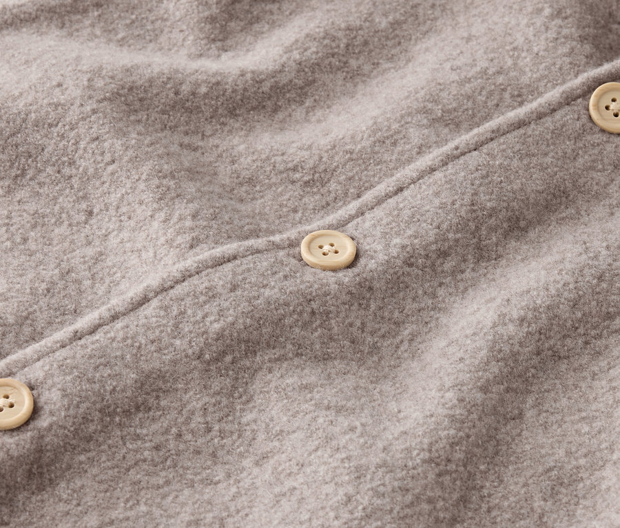 Nahaufnahme eines grauen Wollstoffes mit drei beigen Knöpfen.
