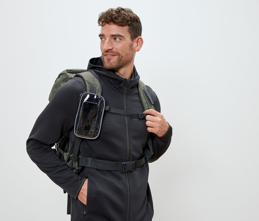Mann mit olivgrünem Rucksack und durchsichtiger Handytasche an den Trägern.