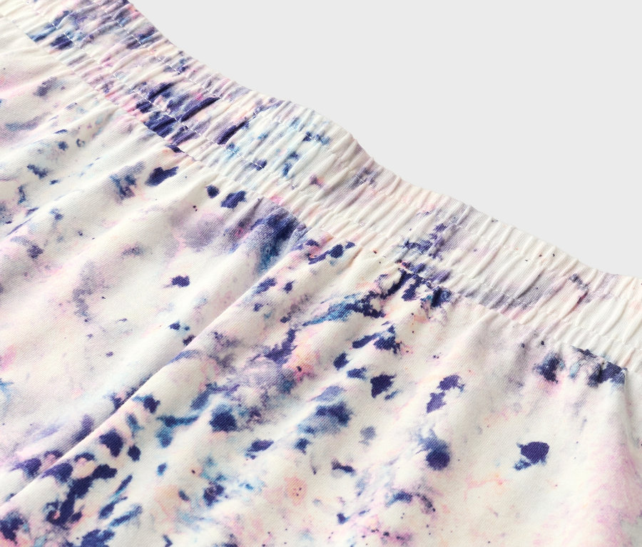 Nahaufnahme von Shorts mit elastischem Bund und Batikmuster in Lila, Blau und Rosa.