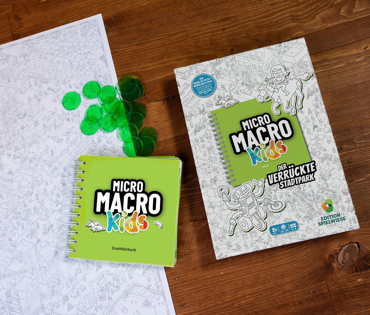 Auf einem Holztisch liegen das Spiel MicroMacro Kids »Der verrückte Stadtpark«, ein Ermittlerbuch, grüne Chips und ein Stadtplan.