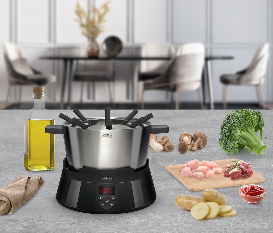 Auf einem Tisch steht ein CASO Induktions-Fondue mit Zutaten wie Fleisch, Pilzen und Gemüse.