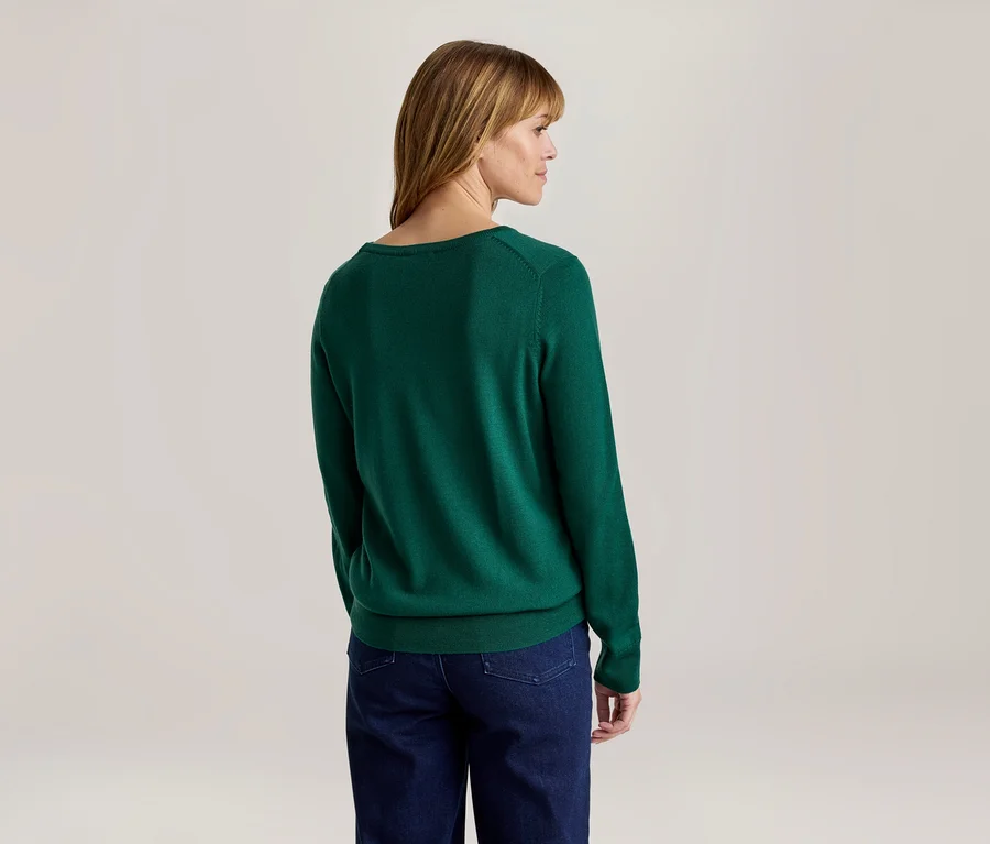 Frau von hinten, leicht nach rechts gedreht, trägt einen grünen Langarmpullover und eine dunkelblaue Jeans.