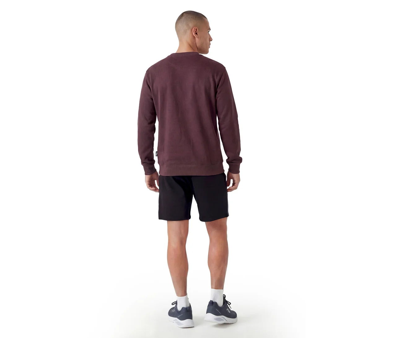 Mann steht mit dem Rücken zum Betrachter, trägt ein bordeauxrotes Rundhals-Sweatshirt, schwarze Shorts, weiße Socken und dunkle Sportschuhe.
