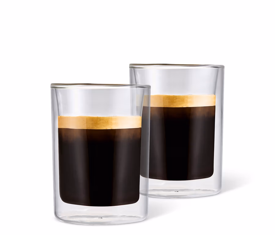 Zwei mit Kaffee gefüllte Caffè Crema Gläser mit Schaum vor einem weißen Hintergrund.
