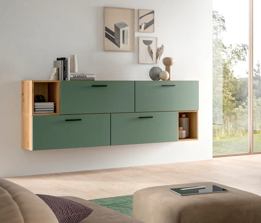 Wandmontiertes modulares Aufbewahrungsmöbel mit grünen Schubladenfronten und hellen Holzregalen in einem Wohnzimmer. Bücher und dekorative Vasen stehen auf und in der Einheit. Ein großes Fenster mit Blick ins Grüne ist rechts, mit einem Sofa und Ottoman im Vordergrund.