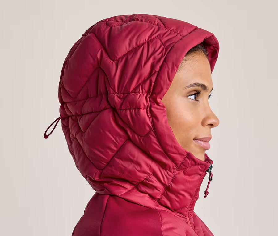 Frau im Profil, die eine pinkfarbene, gesteppte Jacke mit hochgezogener Kapuze trägt und nach rechts blickt.