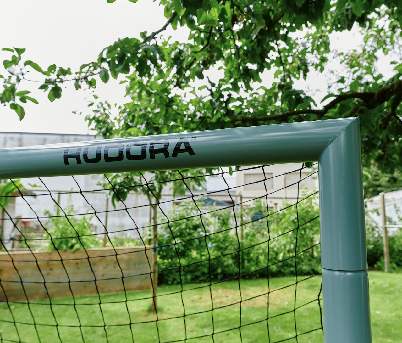 Nahaufnahme des hellgrünen HUDORA Fußballtor Expert 300 mit schwarzem Netz in einem Garten mit grünen Pflanzen und Ästen.