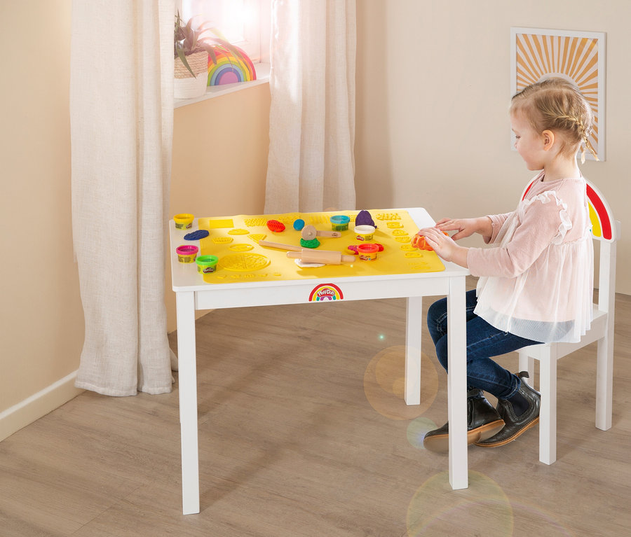 Mädchen spielt am roba x Play-Doh Sitzgruppen-Set mit Knete und Förmchen auf gelber Unterlage.