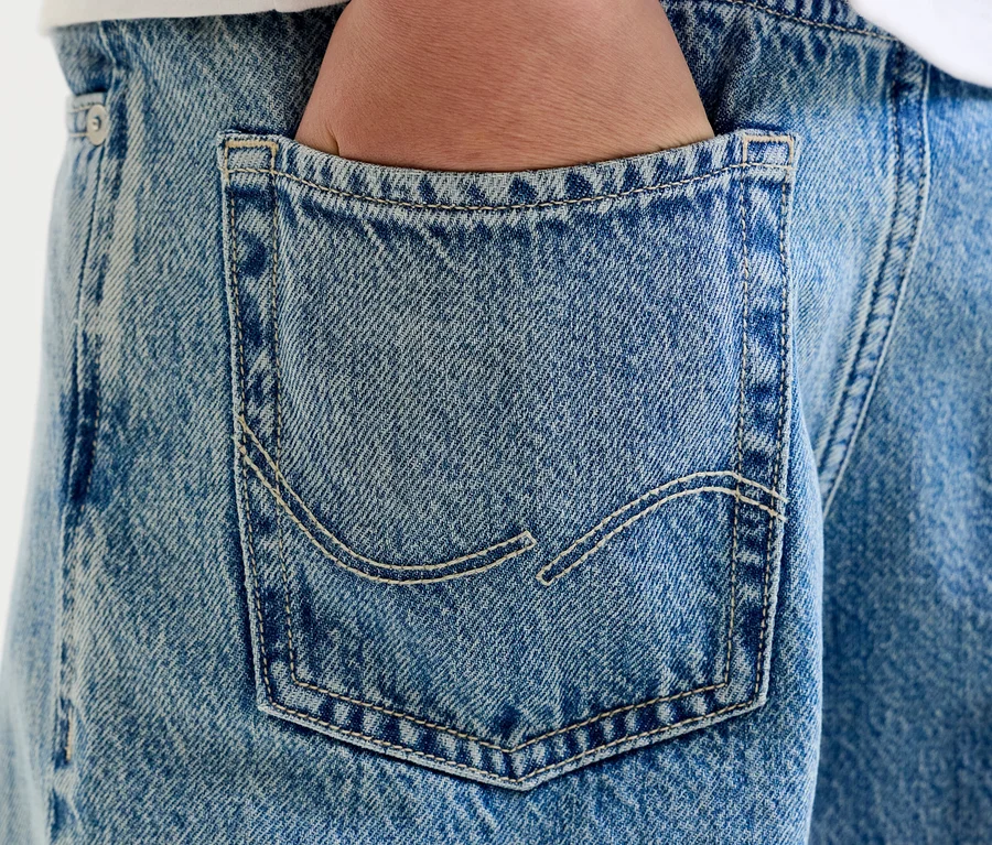 Nahaufnahme einer Hand in der Gesäßtasche einer hellblauen Jeans mit sichtbaren Nähten.
