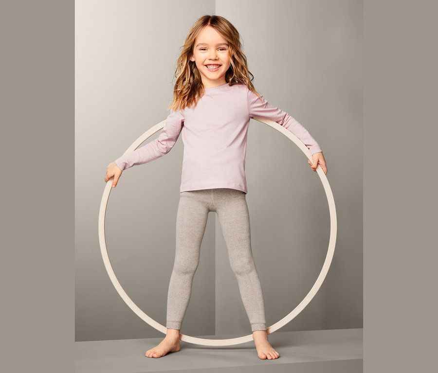 Lächelndes Mädchen hält einen Reifen. Sie trägt ein rosa Shirt und graue 2 Thermoleggings.