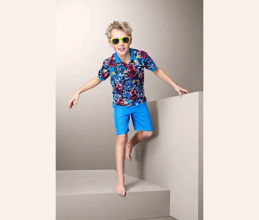Junge posiert in Hawaii-Poloshirt und blauen Shorts.
