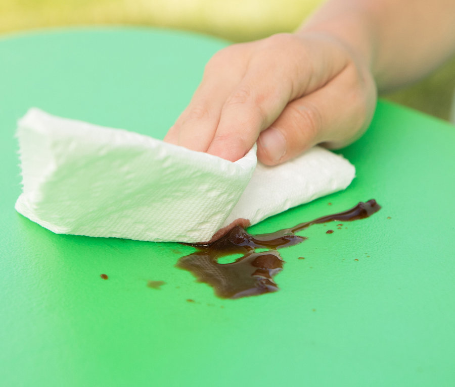 Eine Hand wischt mit einem Tuch verschüttete Flüssigkeit auf einem grünen LIFETIME-Kinder-Picknicktisch ab.