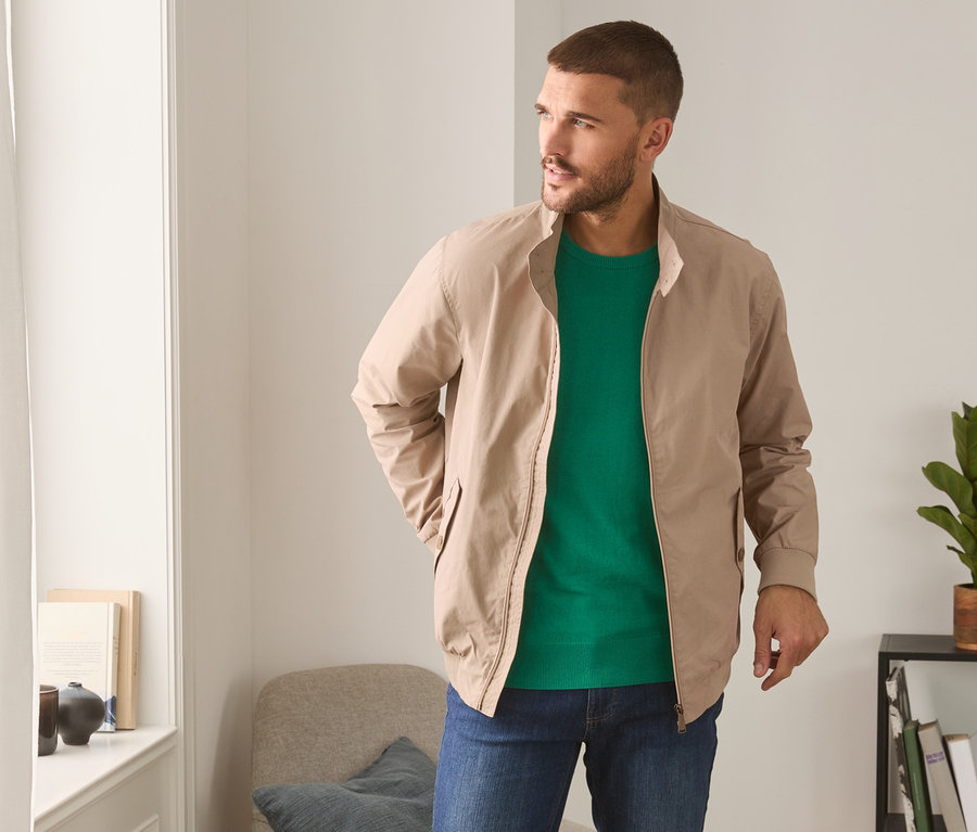 Mann trägt eine beige Blouson, ein grünes T-Shirt und Jeans.