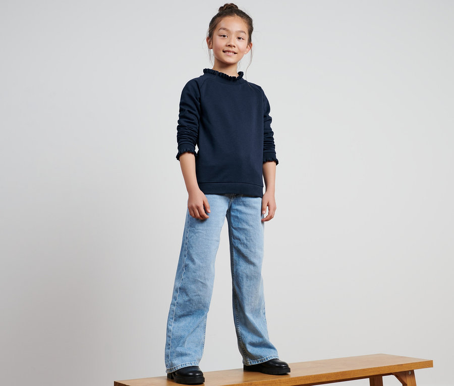 Mädchen steht auf einer Bank und trägt ein Kinder-Sweatshirt.