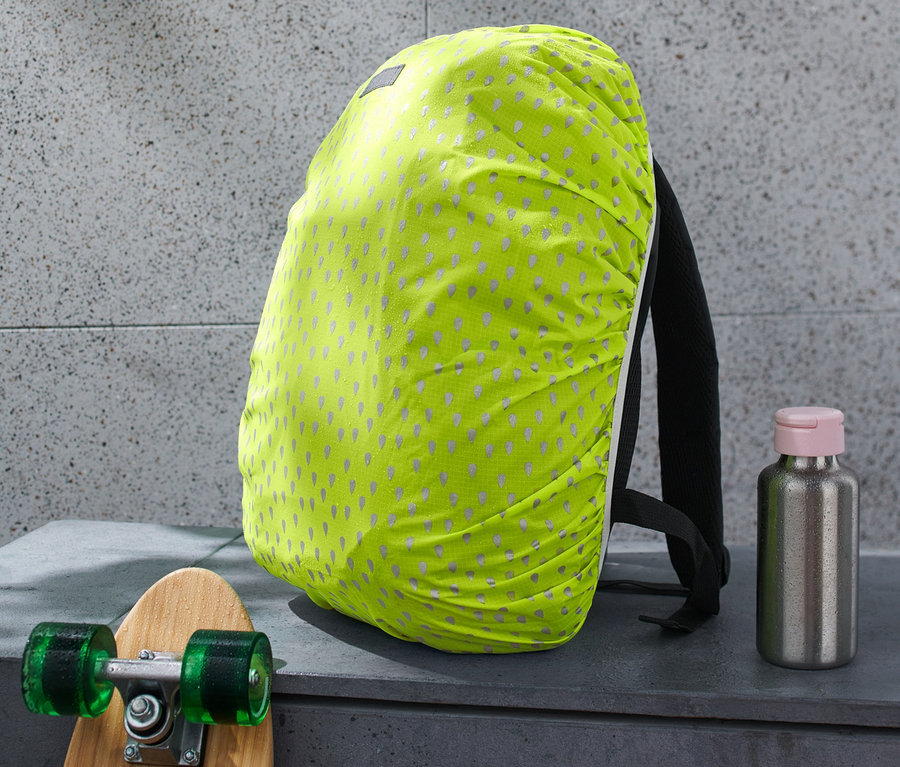 Rucksack mit reflektierendem Regenschutz, daneben ein Skateboard und eine Trinkflasche.